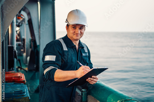 Deck Officer on deck of offshore vessel or ship , wearing PPE personal protective equipment. He fills checklist. Paperwork at sea photo