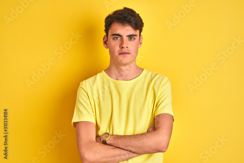 Teenager boy wearing yellow t-shirt over isolated background skeptic and nervous, disapproving expression on face with crossed arms. Negative person.