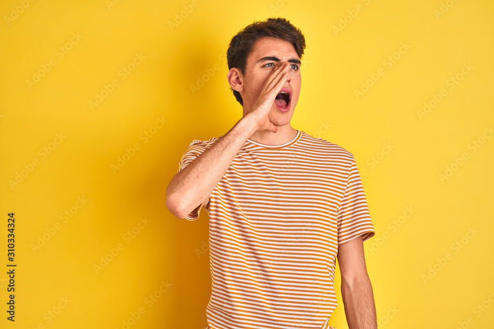 Teenager boy wearing yellow t-shirt over isolated background shouting and screaming loud to side with hand on mouth. Communication concept. Teenager boy wearing yellow t-shirt over isolated background shouting and screaming loud to side with hand on mouth. Communication concept.