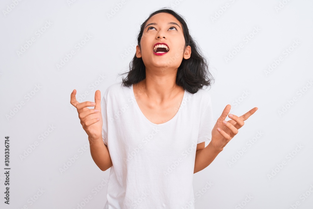 Young chinese woman wearing casual t-shirt standing over isolated white background crazy and mad shouting and yelling with aggressive expression and arms raised. Frustration concept.