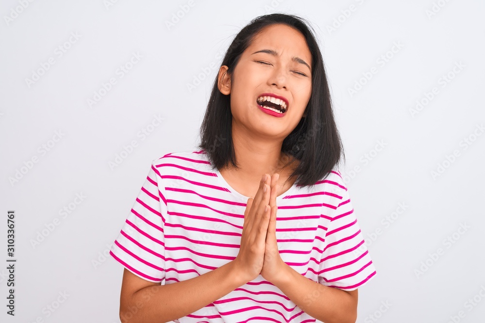 Young chinese woman wearing striped t-shirt standing over isolated white background begging and praying with hands together with hope expression on face very emotional and worried. Asking Young chinese woman wearing striped t-shirt standing over isolated white background begging and praying with hands together with hope expression on face very emotional and worried. Asking