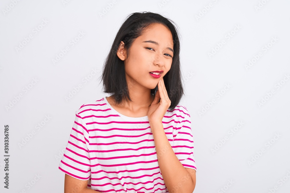 Young chinese woman wearing striped t-shirt standing over isolated white background touching mouth with hand with painful expression because of toothache or dental illness on teeth. Dentist concept. Young chinese woman wearing striped t-shirt standing over isolated white background touching mouth with hand with painful expression because of toothache or dental illness on teeth. Dentist concept.