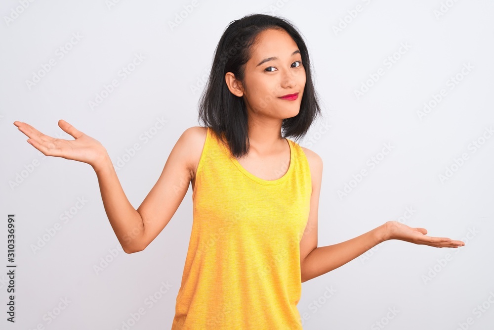 Young chinese woman wearing yellow casual t-shirt standing over isolated white background clueless and confused expression with arms and hands raised. Doubt concept. Young chinese woman wearing yellow casual t-shirt standing over isolated white background clueless and confused expression with arms and hands raised. Doubt concept.