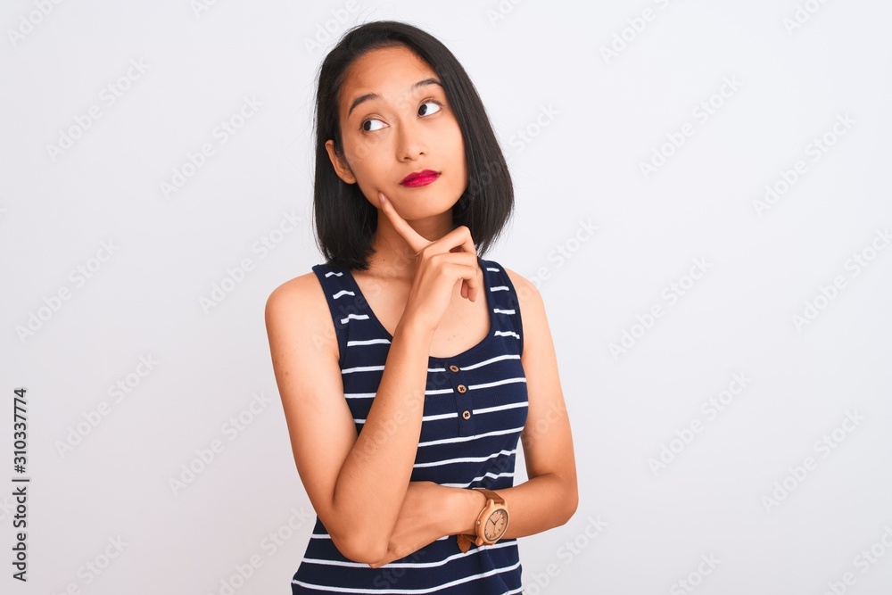 Young chinese woman wearing striped t-shirt standing over isolated white background with hand on chin thinking about question, pensive expression. Smiling with thoughtful face. Doubt concept. Young chinese woman wearing striped t-shirt standing over isolated white background with hand on chin thinking about question, pensive expression. Smiling with thoughtful face. Doubt concept.
