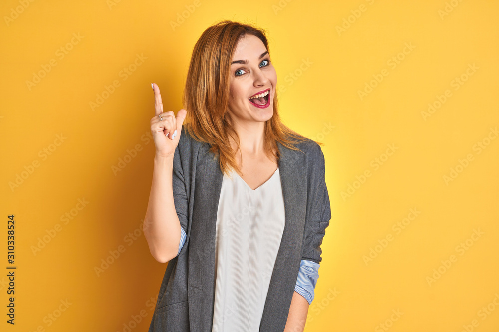 Redhead caucasian business woman over yellow isolated background pointing finger up with successful idea. Exited and happy. Number one. - obrazy, fototapety, plakaty 