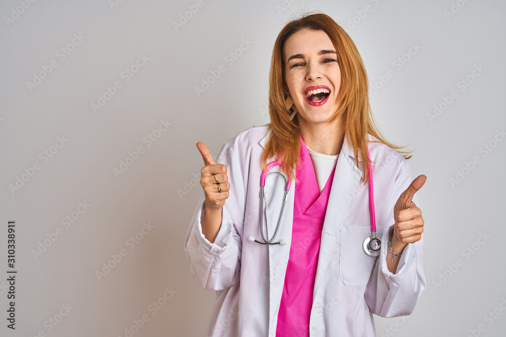 Redhead caucasian doctor woman wearing pink stethoscope over isolated background success sign doing positive gesture with hand, thumbs up smiling and happy. Cheerful expression and winner gesture. Redhead caucasian doctor woman wearing pink stethoscope over isolated background success sign doing positive gesture with hand, thumbs up smiling and happy. Cheerful expression and winner gesture.