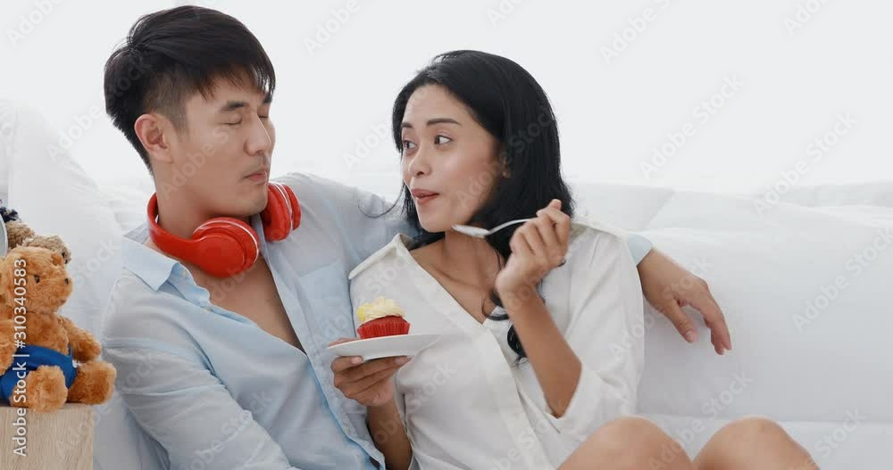 Asian couple is in pajamas. They are sitting in the bedroom. The woman feeds her cupcakes to her boyfriend. It is a happy time. Asian couple is in pajamas. They are sitting in the bedroom. The woman feeds her cupcakes to her boyfriend. It is a happy time.