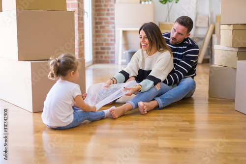 Beautiful family sitting on the floor playing with his kid at new home around cardboard boxes