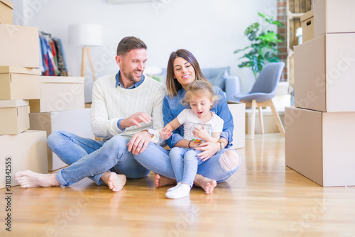 Beautiful family sitting on the floor playing with his kid at new home around cardboard boxes