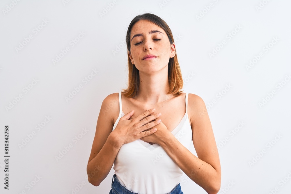 Beautiful redhead woman wearing casual white t-shirt over isolated background smiling with hands on chest with closed eyes and grateful gesture on face. Health concept. Beautiful redhead woman wearing casual white t-shirt over isolated background smiling with hands on chest with closed eyes and grateful gesture on face. Health concept.
