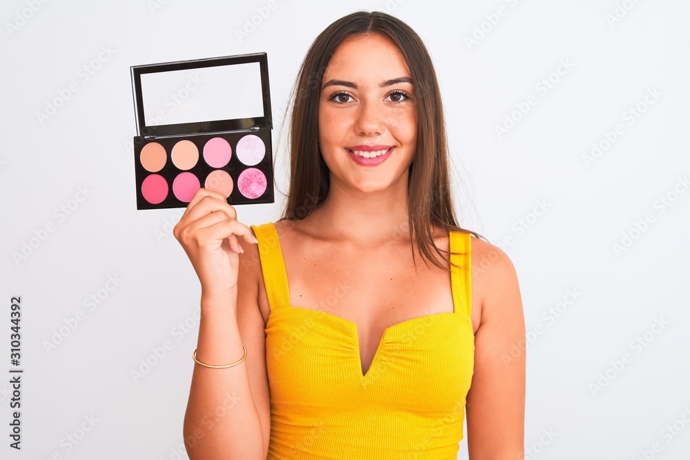 Young beautiful girl holding makeup standing over isolated white background with a happy face standing and smiling with a confident smile showing teeth Young beautiful girl holding makeup standing over isolated white background with a happy face standing and smiling with a confident smile showing teeth