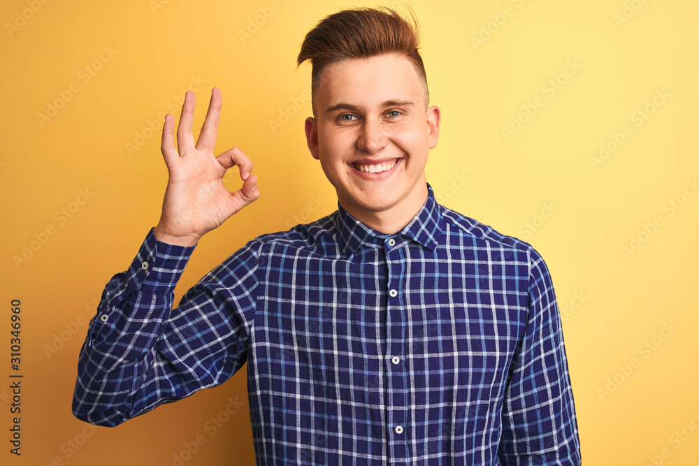Young handsome man wearing casual shirt standing over isolated yellow background smiling positive doing ok sign with hand and fingers. Successful expression. Young handsome man wearing casual shirt standing over isolated yellow background smiling positive doing ok sign with hand and fingers. Successful expression.
