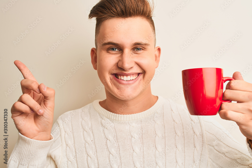 Young handsome man drinking red cup of coffee standing over isolated white background very happy pointing with hand and finger to the side Young handsome man drinking red cup of coffee standing over isolated white background very happy pointing with hand and finger to the side