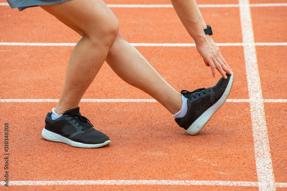 Cropped shot view of runner woman doing stretching and warming up her legs before running in the running track in stadium. The benifit of stretching can increasing flexibility and reduce injury. Cropped shot view of runner woman doing stretching and warming up her legs before running in the running track in stadium. The benifit of stretching can increasing flexibility and reduce injury.