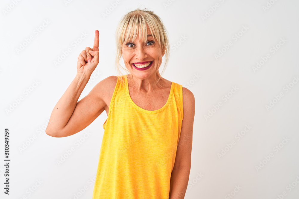 Middle age woman wearing yellow casual t-shirt standing over isolated white background pointing finger up with successful idea. Exited and happy. Number one. Middle age woman wearing yellow casual t-shirt standing over isolated white background pointing finger up with successful idea. Exited and happy. Number one.