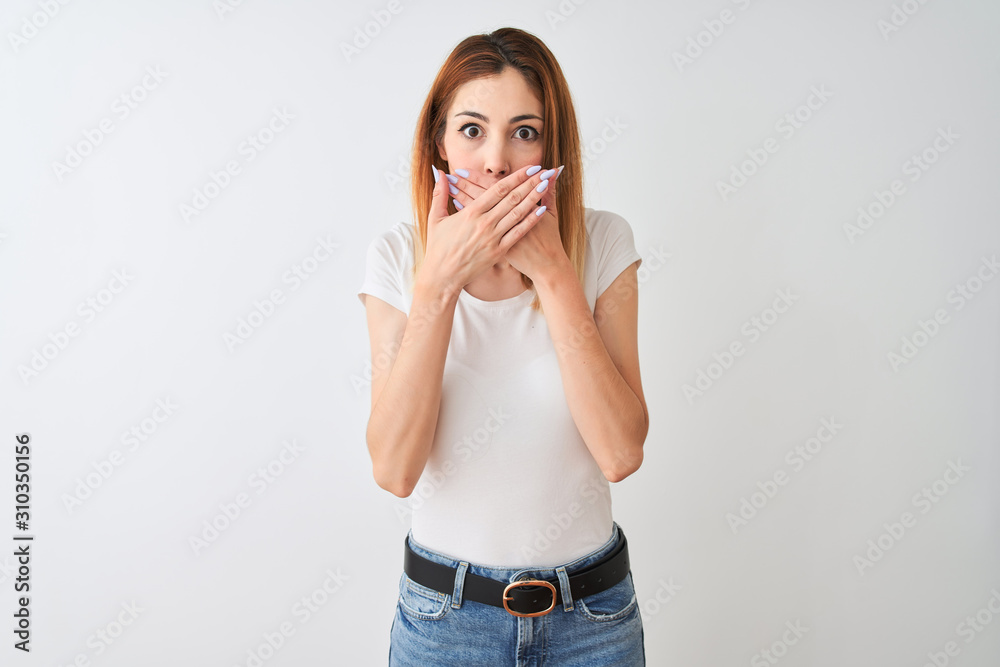 Beautiful redhead woman wearing casual t-shirt standing over isolated white background shocked covering mouth with hands for mistake. Secret concept. Beautiful redhead woman wearing casual t-shirt standing over isolated white background shocked covering mouth with hands for mistake. Secret concept.