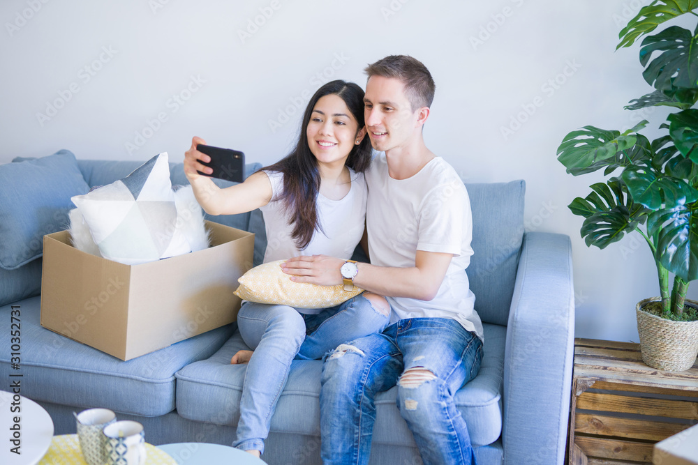 Young beautiful couple sitting on the sofa using smartphone to take a selfie at new home around cardboard boxes Young beautiful couple sitting on the sofa using smartphone to take a selfie at new home around cardboard boxes