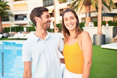 Young beautiful couple on vacation smiling happy and confident. Standing with smile on face hugging at the beach club