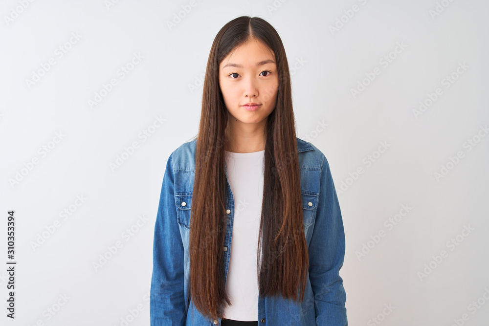 Young chinese woman wearing denim shirt standing over isolated white background Relaxed with serious expression on face. Simple and natural looking at the camera. Young chinese woman wearing denim shirt standing over isolated white background Relaxed with serious expression on face. Simple and natural looking at the camera.