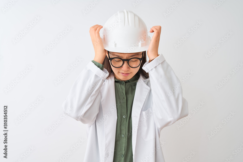 Young chinese engineer woman wearing coat helmet glasses over isolated white background suffering from headache desperate and stressed because pain and migraine. Hands on head. Young chinese engineer woman wearing coat helmet glasses over isolated white background suffering from headache desperate and stressed because pain and migraine. Hands on head.