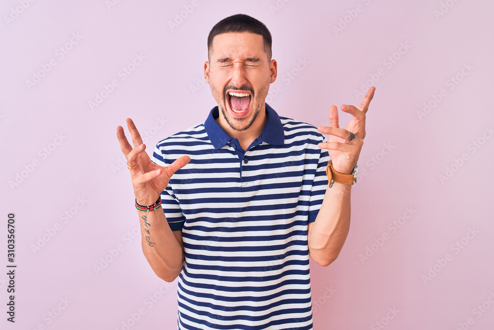 Young handsome man wearing nautical striped t-shirt over pink isolated background celebrating mad and crazy for success with arms raised and closed eyes screaming excited. Winner concept