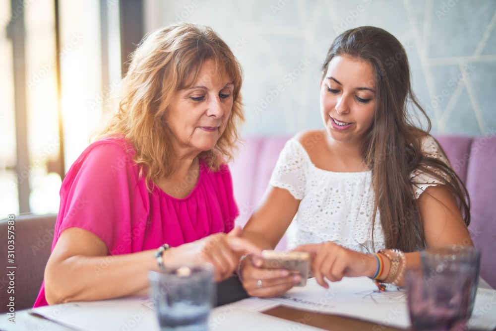 Beautiful mother and daugther sitting at restaurant using smartphone smiling Beautiful mother and daugther sitting at restaurant using smartphone smiling