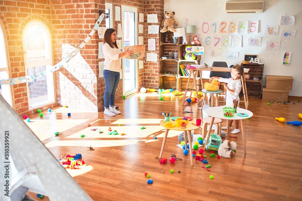 Obraz premium Beautiful teacher and toddler playing basketball using ball and wicker basket around lots of toys at kindergarten