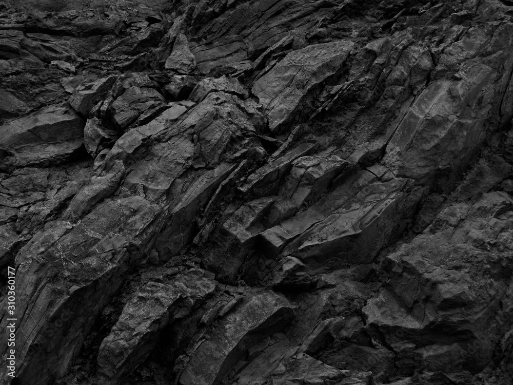Black white rock background. Dark gray stone texture.  Mountain surface close-up. Distressed, сracked, collapsed, crumbled, broken. 