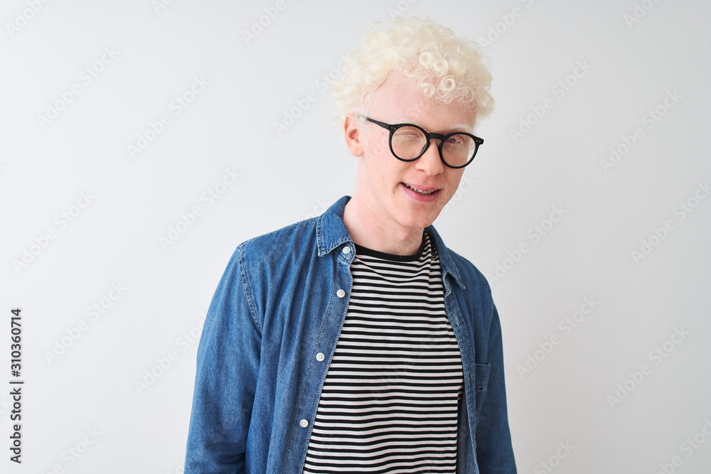 Young albino blond man wearing denim shirt and glasses over isolated white background winking looking at the camera with sexy expression, cheerful and happy face. Young albino blond man wearing denim shirt and glasses over isolated white background winking looking at the camera with sexy expression, cheerful and happy face.