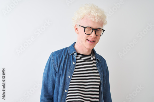 Young albino blond man wearing denim shirt and glasses over isolated white background winking looking at the camera with sexy expression, cheerful and happy face.