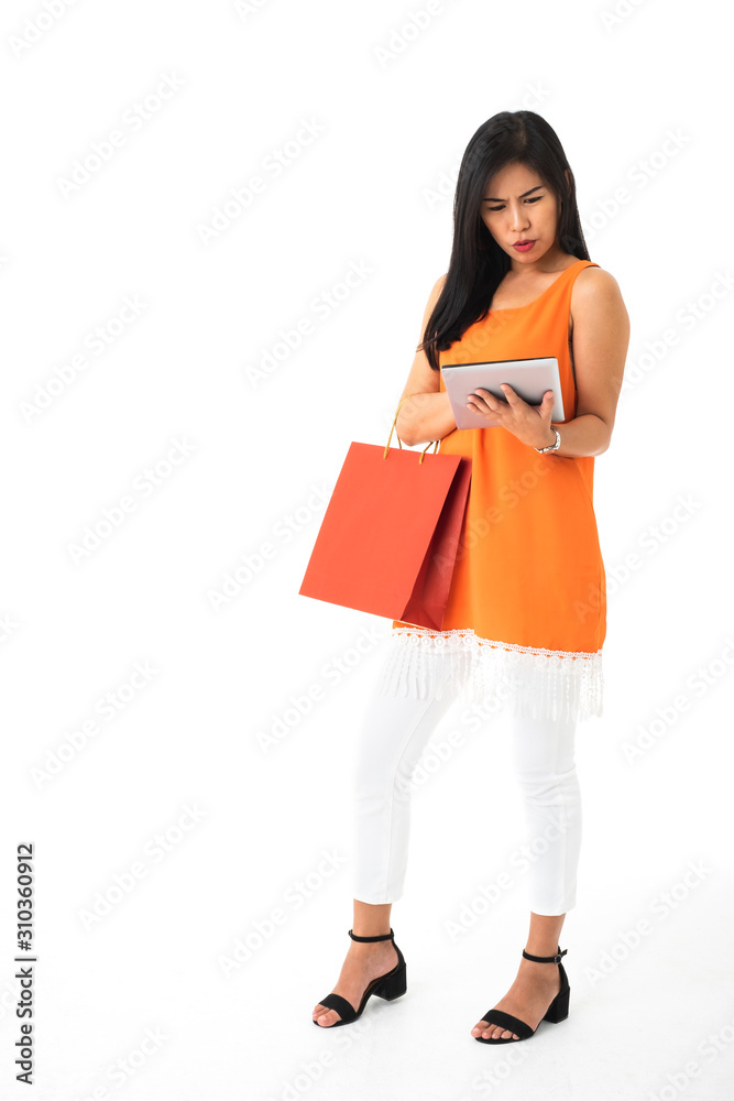 A beautiful Asian young woman wearing orange dress holding a tablet and a shopping bag looking frustrated or confuse in front of white isolated background. A beautiful Asian young woman wearing orange dress holding a tablet and a shopping bag looking frustrated or confuse in front of white isolated background.