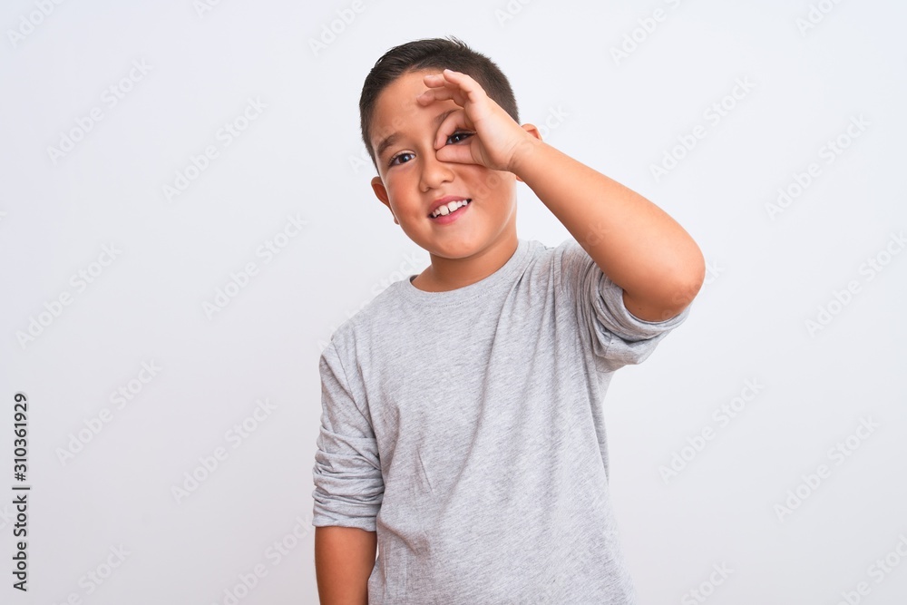 Beautiful kid boy wearing grey casual t-shirt standing over isolated white background doing ok gesture with hand smiling, eye looking through fingers with happy face. Beautiful kid boy wearing grey casual t-shirt standing over isolated white background doing ok gesture with hand smiling, eye looking through fingers with happy face.