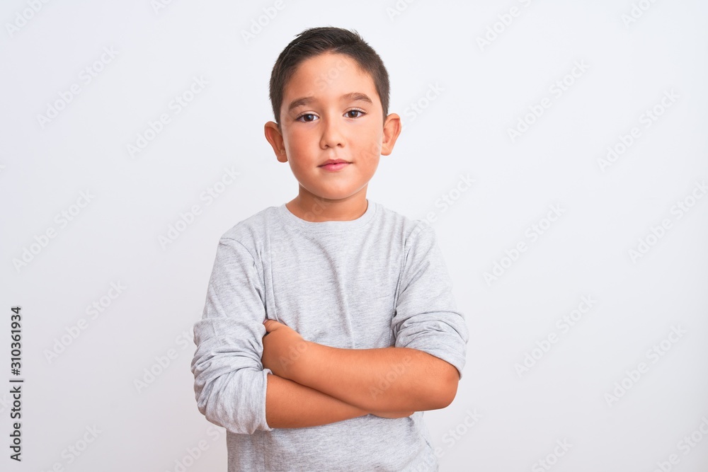 Beautiful kid boy wearing grey casual t-shirt standing over isolated white background with serious expression on face. Simple and natural looking at the camera. Beautiful kid boy wearing grey casual t-shirt standing over isolated white background with serious expression on face. Simple and natural looking at the camera.
