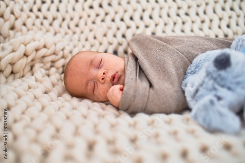 Adorable baby lying down on the sofa over blanket at home. Newborn relaxing and sleeping comfortable