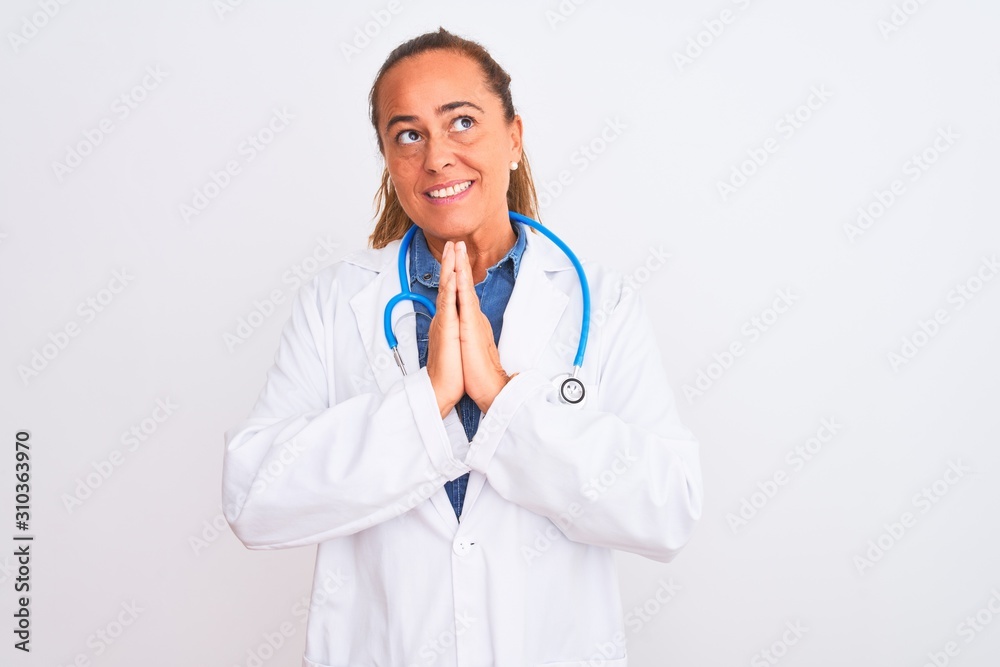 Middle age mature doctor woman wearing stethoscope over isolated background praying with hands together asking for forgiveness smiling confident. Middle age mature doctor woman wearing stethoscope over isolated background praying with hands together asking for forgiveness smiling confident.