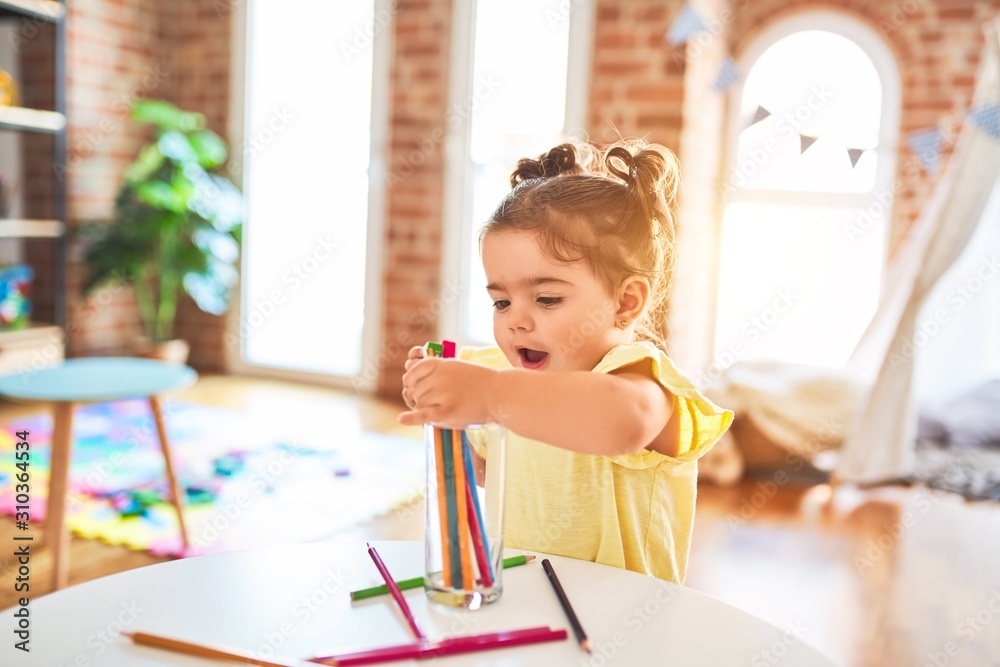Beautiful toddler standing holding colored pencils at kindergarten - obrazy, fototapety, plakaty 