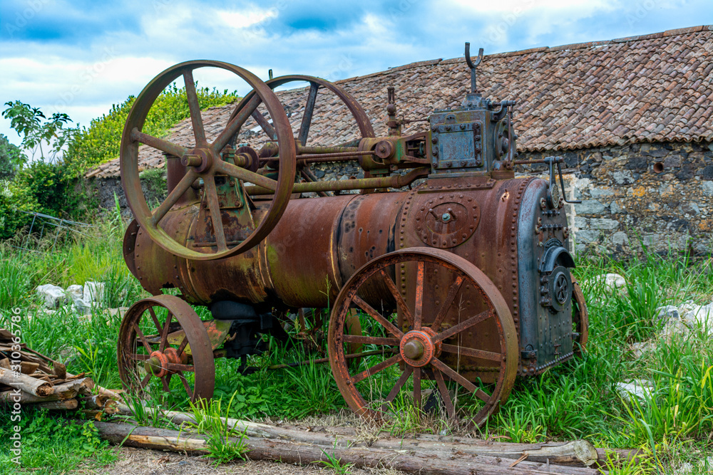 Rusty antique farm equipment next to stone building