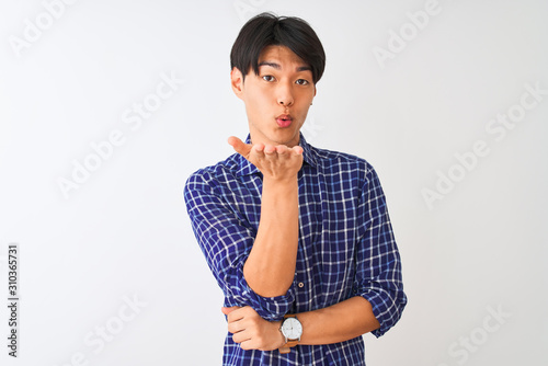 Young chinese man wearing casual blue shirt standing over isolated white background looking at the camera blowing a kiss with hand on air being lovely and sexy. Love expression.