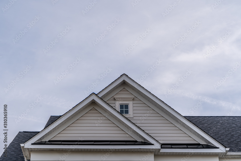 Reverse double gable close up on luxury single family residential home.  Square single pane gable window. Roof line of traditional home with one gable running one way reverse gables running the other.