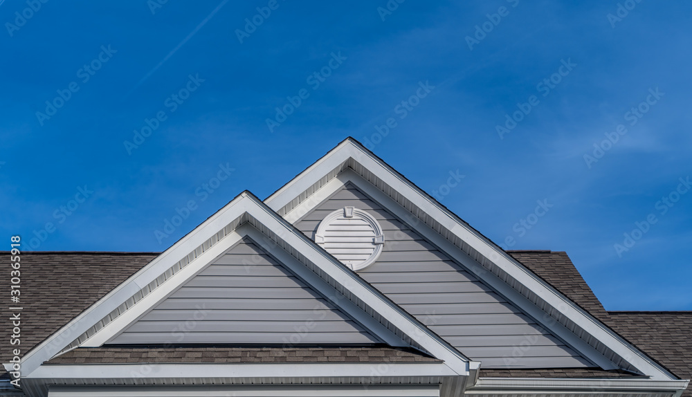 Reverse double gable close up on luxury single family residential home.  White round louver vent. . Roof line of traditional home with one gable running one way reverse gables running the other.