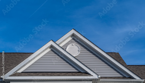 Reverse double gable close up on luxury single family residential home. White round louver vent. . Roof line of traditional home with one gable running one way reverse gables running the other.