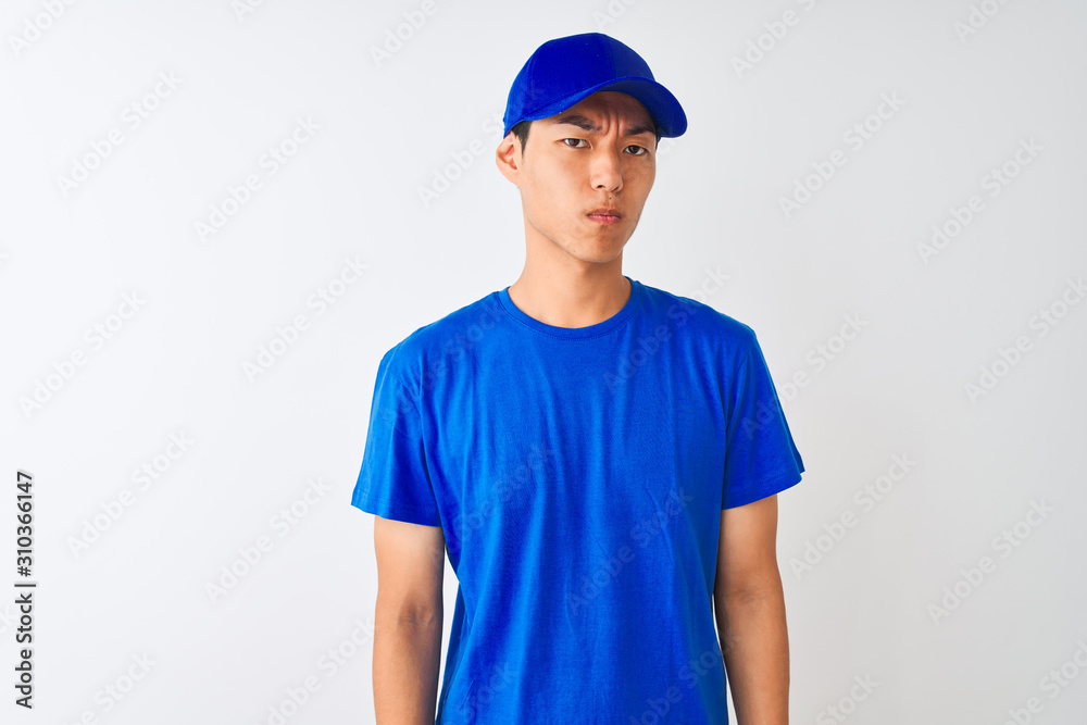Chinese deliveryman wearing blue t-shirt and cap standing over isolated white background skeptic and nervous, frowning upset because of problem. Negative person.