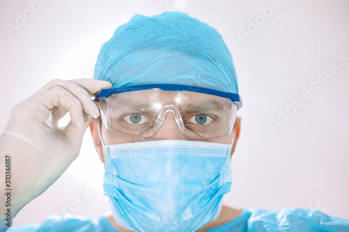 Doctor surgeon in uniform and glasses looks at the camera  the patient back bright light in the operating room.