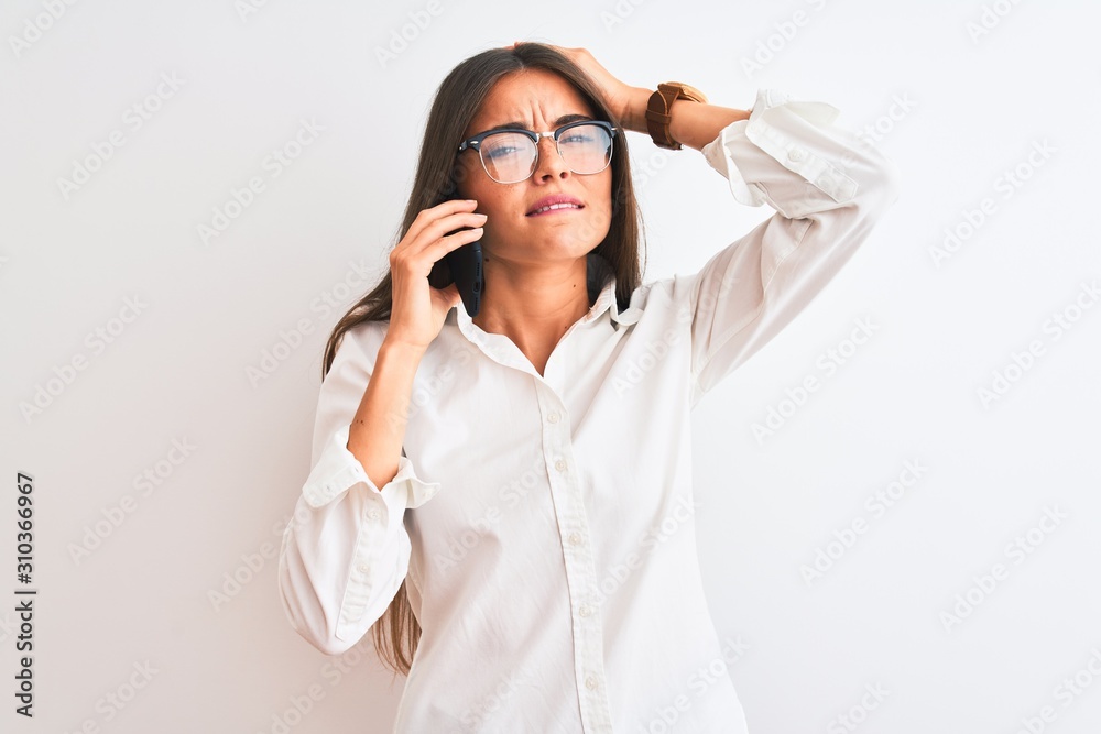 Young businesswoman wearing glasses talking on smartphone over isolated white background stressed with hand on head, shocked with shame and surprise face, angry and frustrated. Fear and upset Young businesswoman wearing glasses talking on smartphone over isolated white background stressed with hand on head, shocked with shame and surprise face, angry and frustrated. Fear and upset