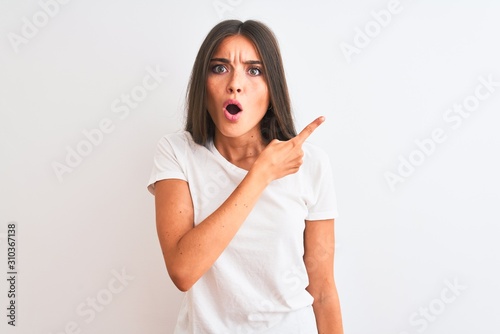 Young beautiful woman wearing casual t-shirt standing over isolated white background Surprised pointing with finger to the side  open mouth amazed expression.