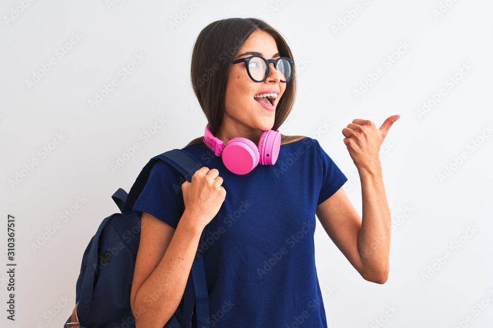 Young student woman wearing backpack glasses headphones over isolated white background pointing and showing with thumb up to the side with happy face smiling Young student woman wearing backpack glasses headphones over isolated white background pointing and showing with thumb up to the side with happy face smiling