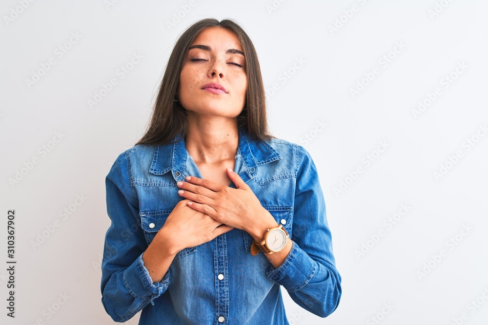 Young beautiful woman wearing casual denim shirt standing over isolated white background smiling with hands on chest with closed eyes and grateful gesture on face. Health concept.
