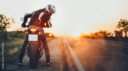 Back view of a amazing young biker looking back at the camera before going to travel on his bike against sunset. photo