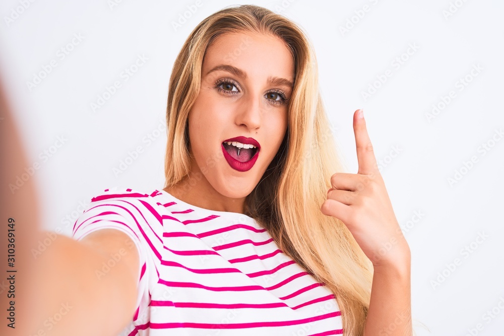 Beautiful woman wearing striped t-shirt make selfie by camera over isolated white background surprised with an idea or question pointing finger with happy face, number one Beautiful woman wearing striped t-shirt make selfie by camera over isolated white background surprised with an idea or question pointing finger with happy face, number one