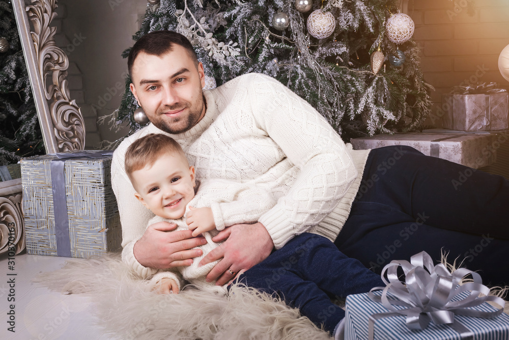 happy handsome father hugging smiling baby son laying on the carpet near the christmas tree